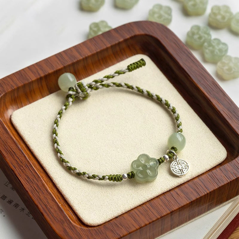 Green braided bracelet with jade plum flower on wooden tray