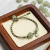Green braided bracelet with jade plum flower on wooden tray