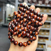 Hand holding a stack of polished natural tiger eye stone bracelets