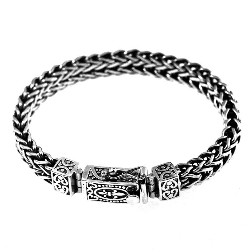 Silver-tone woven copper bracelet with ornate rectangular clasp on wood background
