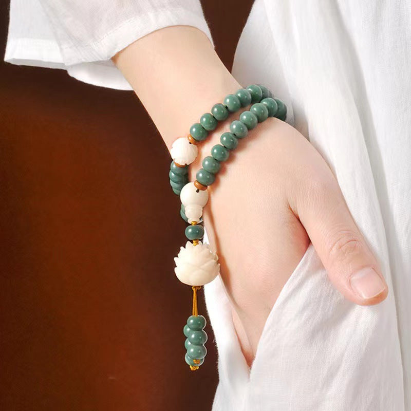 Close up of a green bodhi seed bracelet with a white lotus pendant worn on a wrist