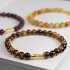 Close up of a brown Tiger Eye bead bracelet with a gold fish charm