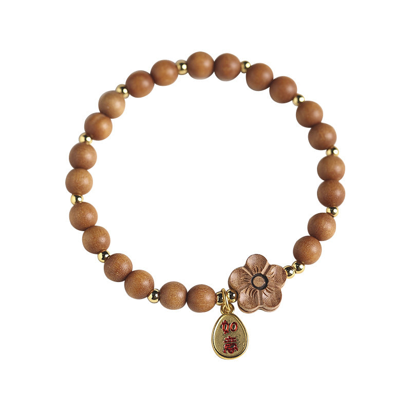 Close-up of a light brown sandalwood bead bracelet with a flower charm on a book