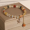 Close-up view of a multicolored rutilated quartz bracelet with a gold-tone zircon flower charm on a beige box