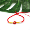 Woven cord bracelet with red flower charm and gold tone copper bead on white background