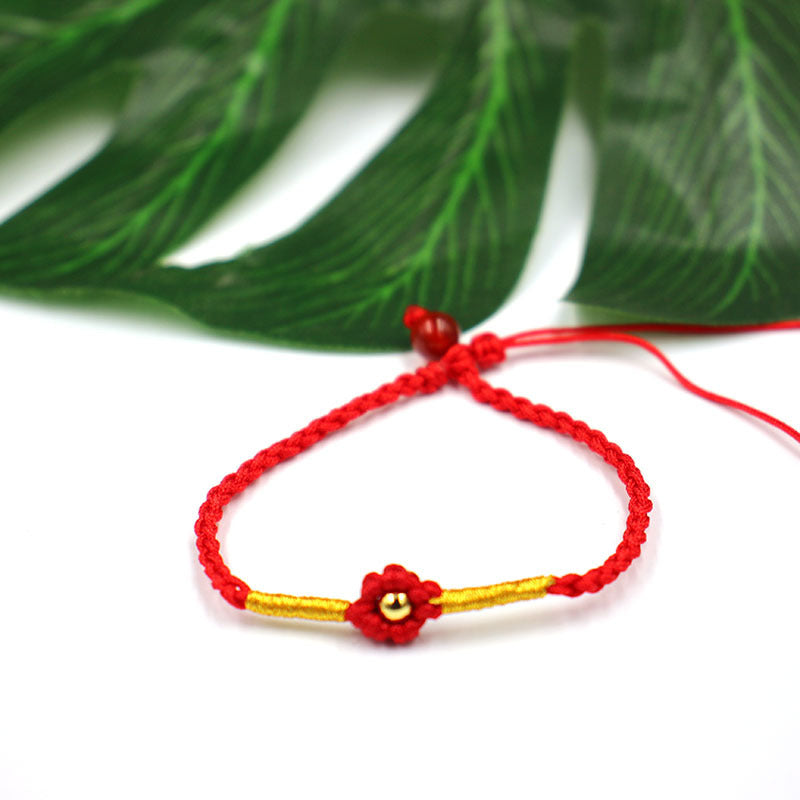 Woven cord bracelet with red flower charm and gold tone copper bead on white background