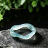Close up of a light blue irregular jade ring on a dark stone surface