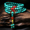 Coiled turquoise mala bracelet with red accents resting on dark wood