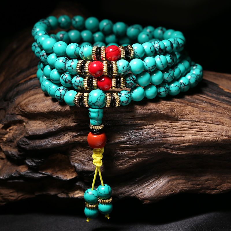 Coiled turquoise mala bracelet with red accents resting on dark wood