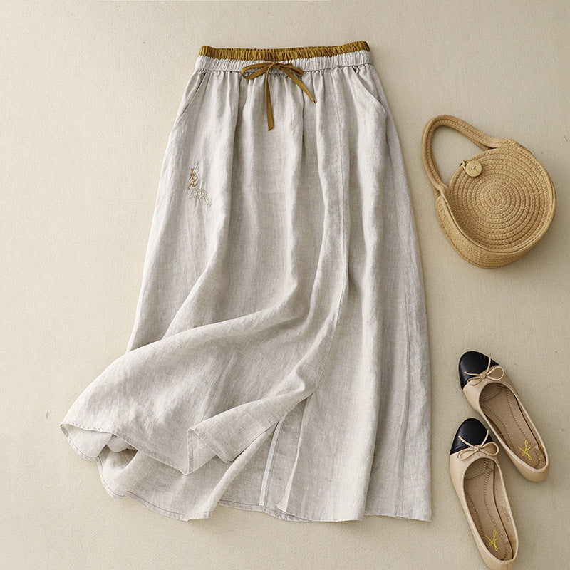 Flat lay of a beige embroidered midi skirt with a drawstring waist next to a woven bag