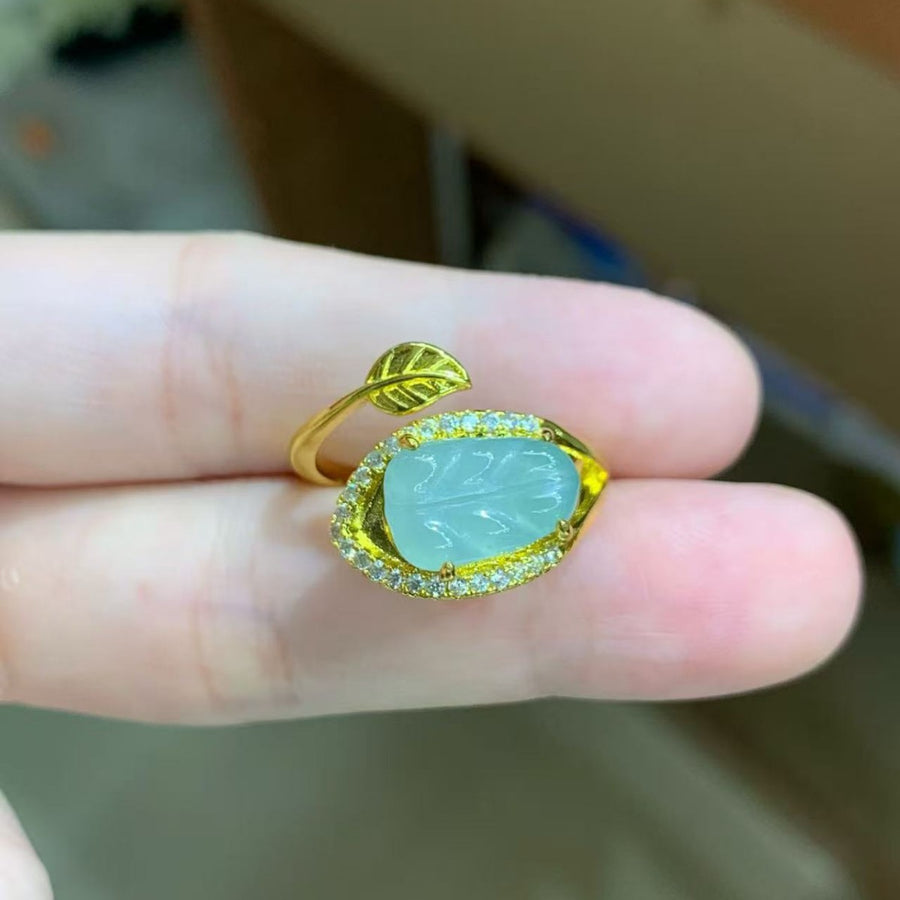 Close-up of an adjustable gold-tone ring with a carved green jade stone and leaf accent held on a finger