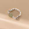 Close up of a sterling silver stretch ring with a single round green jade bead on a beige background