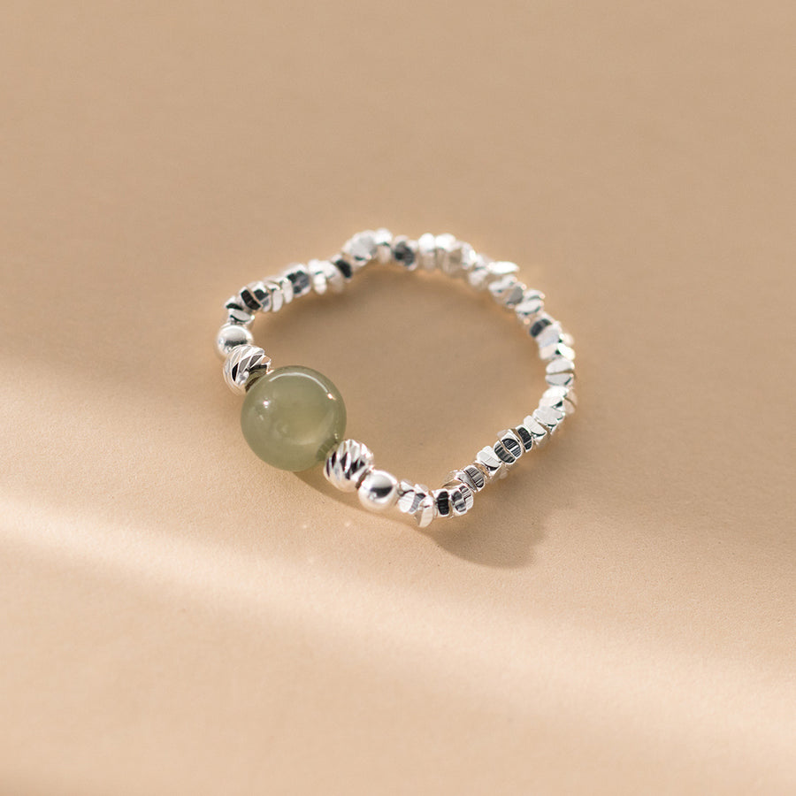 Close up of a sterling silver stretch ring with a single round green jade bead on a beige background