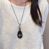 Woman wearing a long necklace with a dark geometric wood and resin pendant