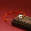 White jade peace buckle bracelet on red woven cord resting on wood