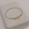 Blue braided cord bracelet with gold-tone coin accents on a display stand