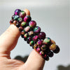 A hand holding strands of multicolored round tiger eye beads showing pink and green shimmer