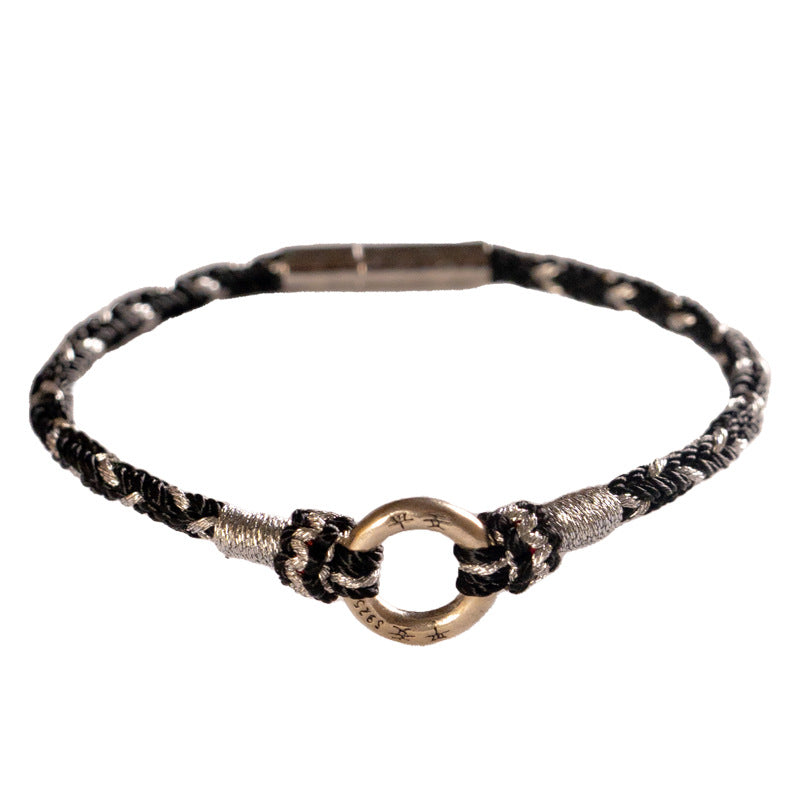 Close up of a black woven cord bracelet with a silver ring charm