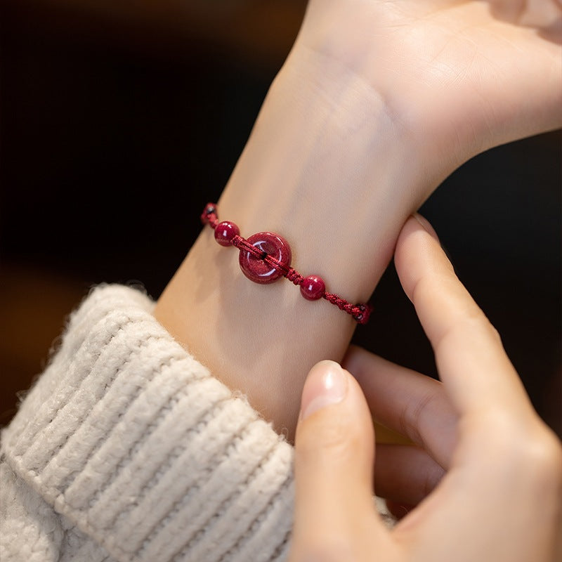 Close up of a red cord bracelet with a cinnabar peace buckle on a wrist