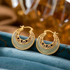 Pair of gold-tone crescent moon hoop earrings with pale green stone accents resting on blue velvet