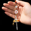 Hand holding a Tibetan style car hanging ornament with a spinning prayer wheel and colorful beads