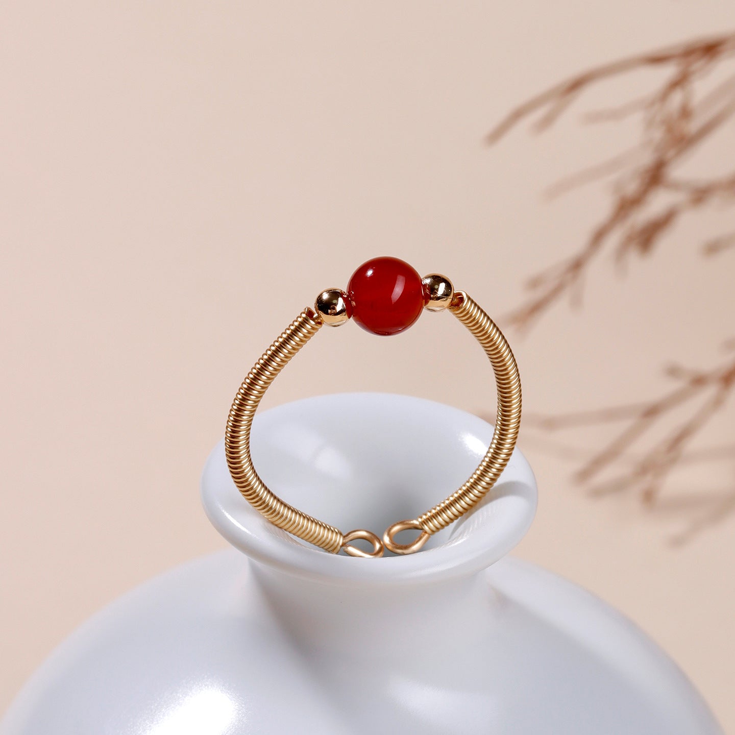 Gold-tone wire open ring with a single red agate bead on a white ceramic stand