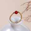 Gold-tone wire open ring with a single red agate bead on a white ceramic stand