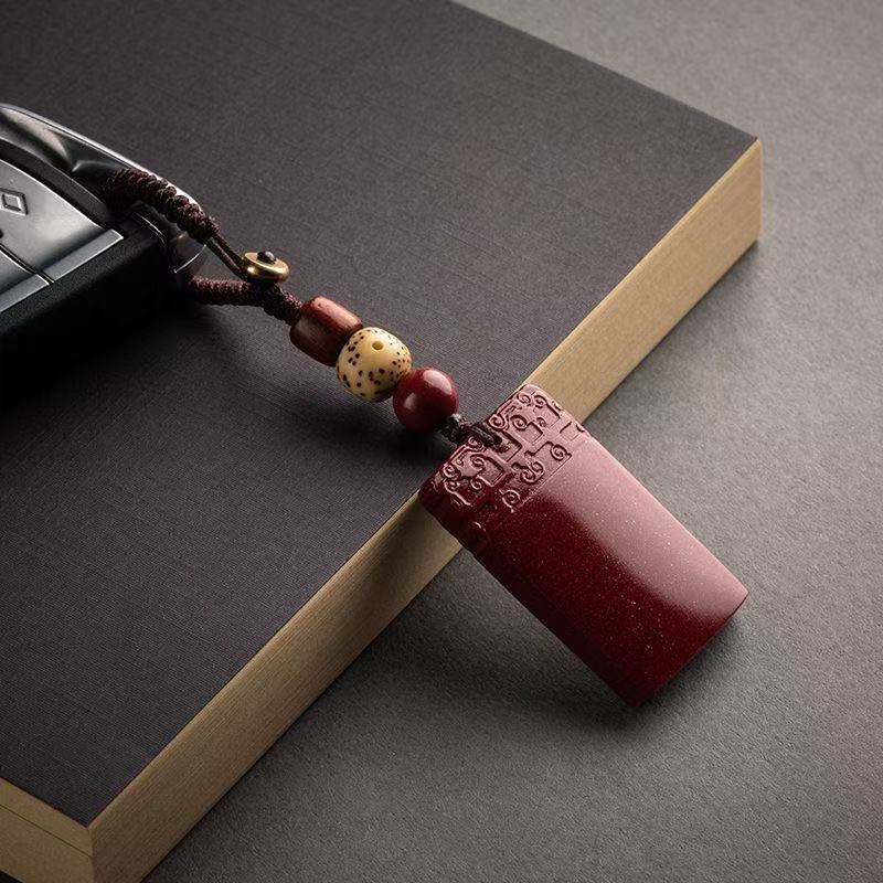 A close-up of a rectangular red cinnabar keychain charm with carved characters resting on a book.