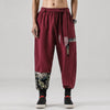 Full view of men wearing loose harem pants in wine red with patterned patches on the legs.