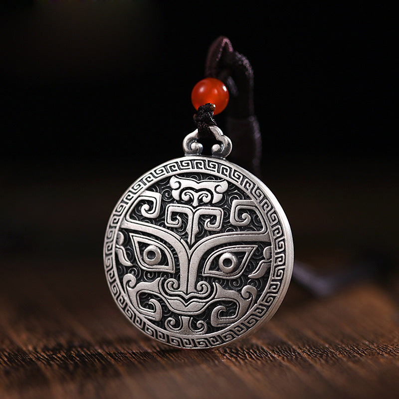 Close up of a round silver tone pendant with a mythical Taotie face design