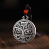 Close up of a round silver tone pendant with a mythical Taotie face design
