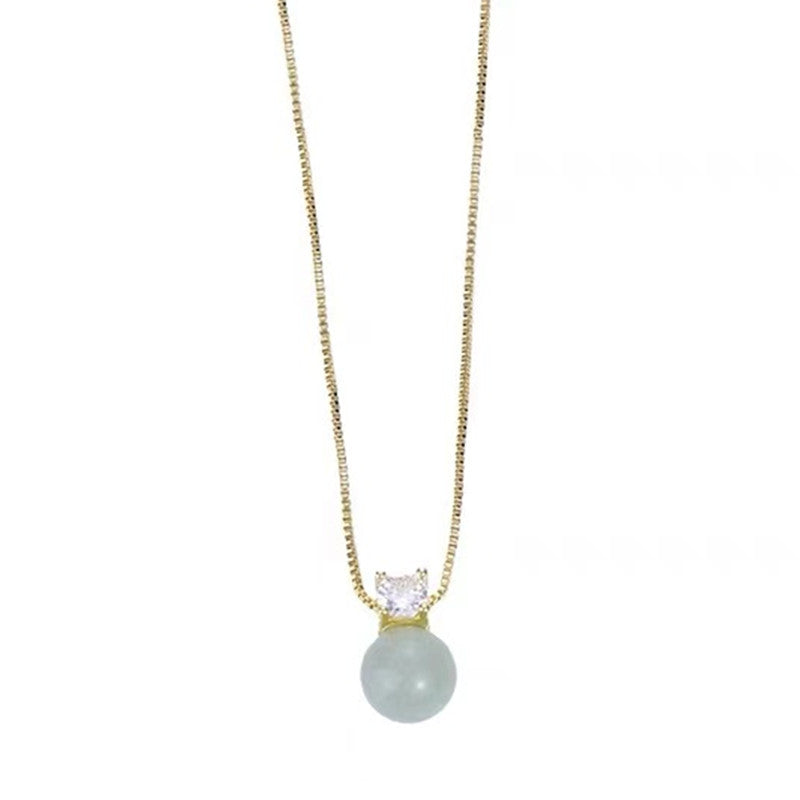 Hand holding a gold necklace with a green jade bead pendant