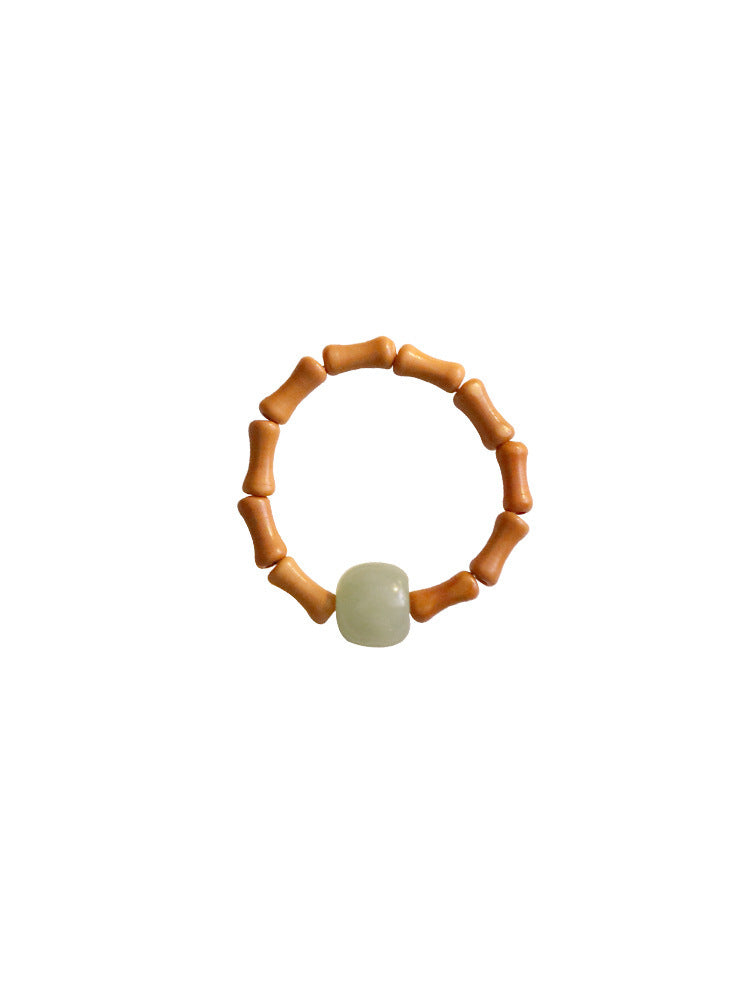 Close up of an adjustable ring with bamboo shaped beads and a pale green jade stone on a white surface