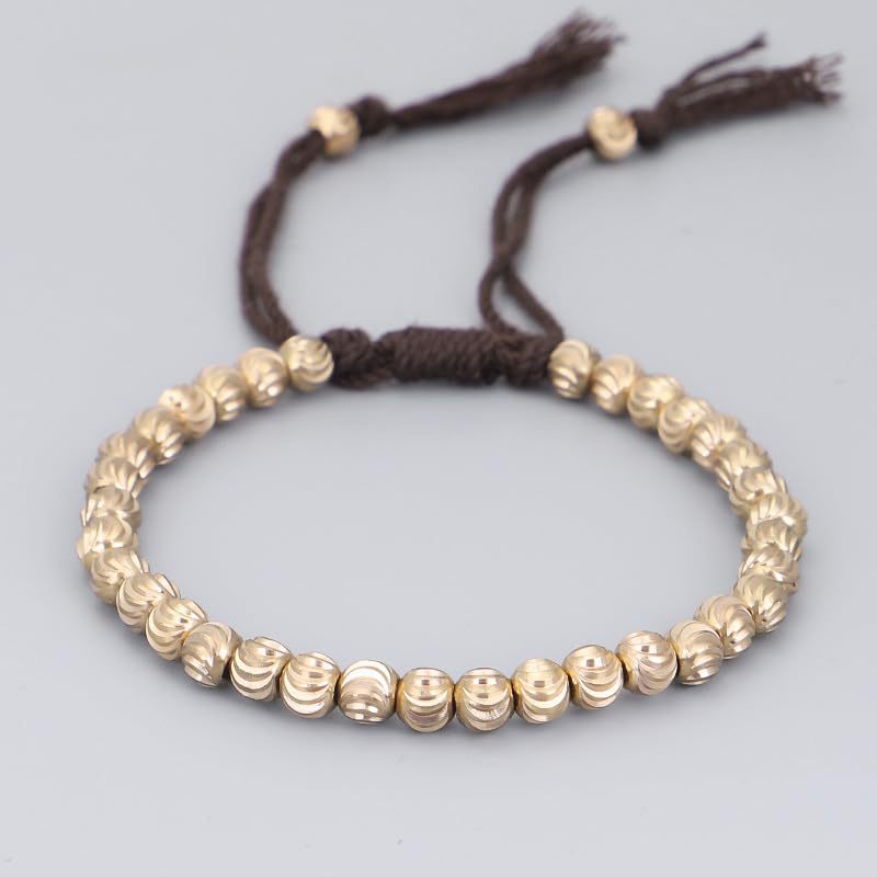 Gold tone copper bead bracelet with brown adjustable cord lying on a white surface