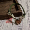 Green braided cord bracelet with a small carved wooden lotus charm resting on a wooden tray