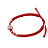 Close up of a silver lotus charm on a red braided bracelet with small silver beads