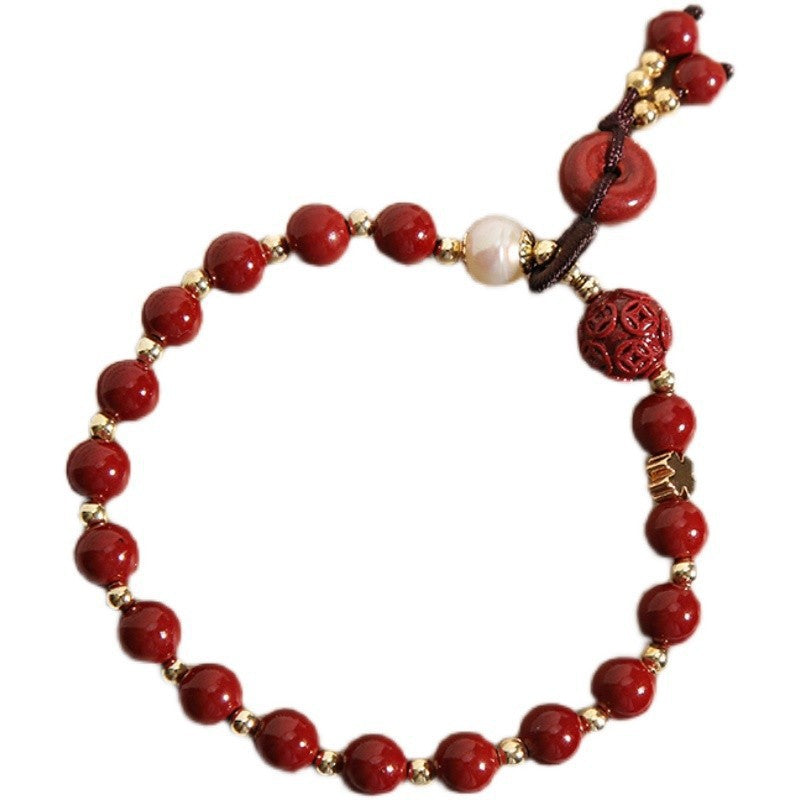 Red cinnabar bead bracelet with gold spacers, a carved clover charm, and a donut-shaped peace buckle pendant.