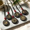 Round black obsidian pendant with gold engraved Buddhist mantras and symbols on a black cord