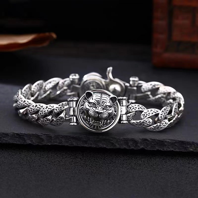 Silver-tone copper bracelet with a rotating tiger head charm on a dark stone surface