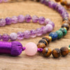 Long beaded necklace with purple tassel and matching bracelet on wood surface