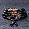 Close up of a coiled black obsidian and tiger eye mala bracelet on a dark surface