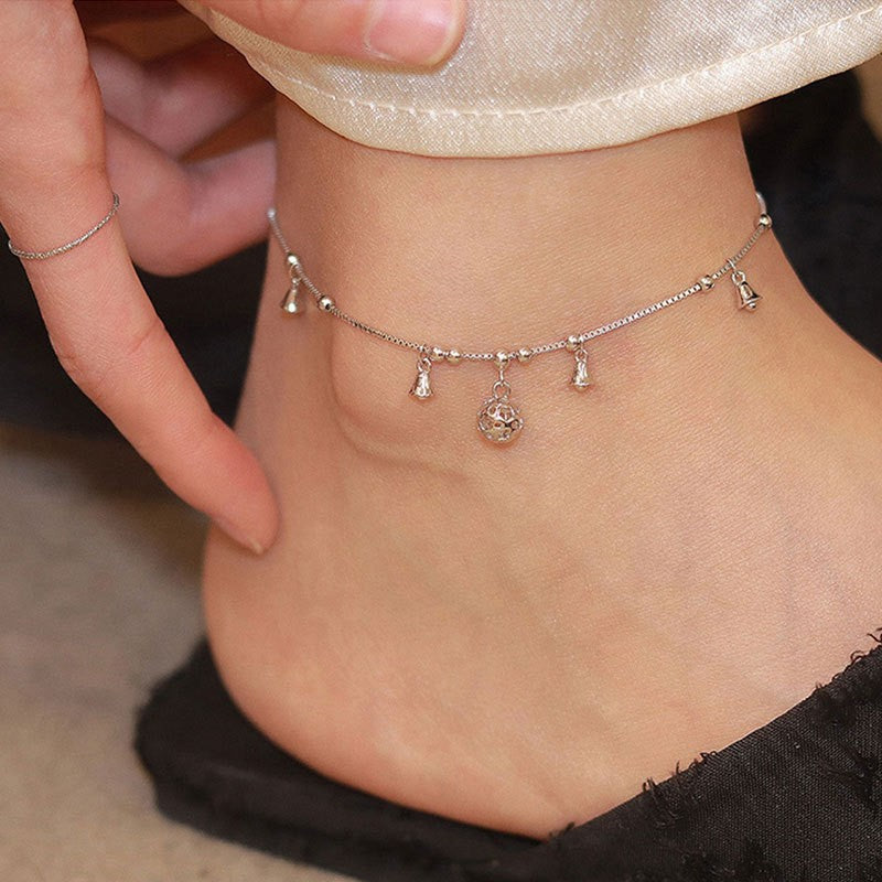 Close up of a silver anklet with small bells and a geometric charm on an ankle