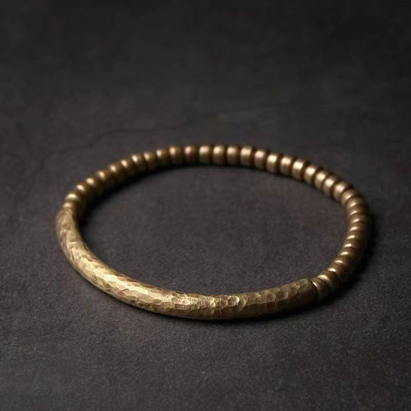 Close up of a handmade copper and brass bead bracelet on a dark surface