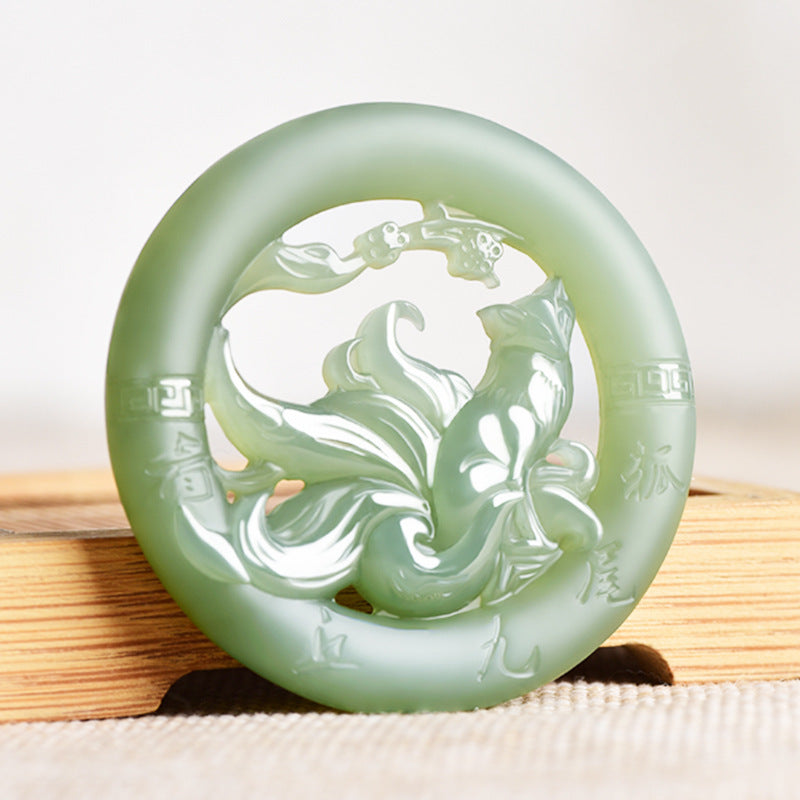 Close up of a round light green jade pendant with a carved nine tailed fox design inside