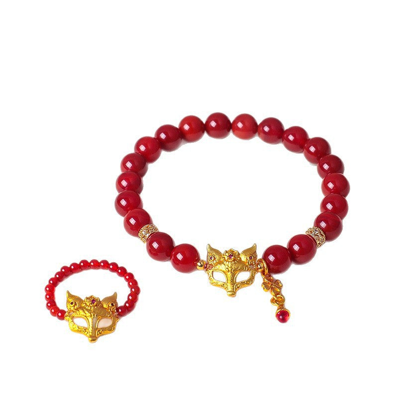 Close up of a red beaded bracelet with a gold fox mask charm on a wrist