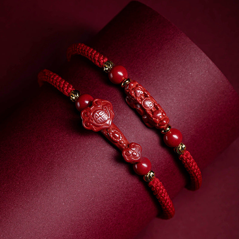 Two red braided bracelets with carved cinnabar charms resting on a dark red surface