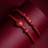 Two red braided bracelets with carved cinnabar charms resting on a dark red surface