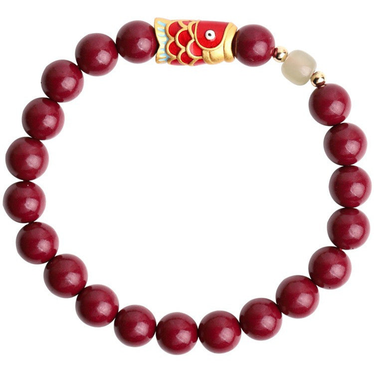 Red cinnabar beaded bracelet with a colorful koi fish charm on a wooden plate