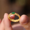 Close up of gold tone ring with green gourd stone held between fingers