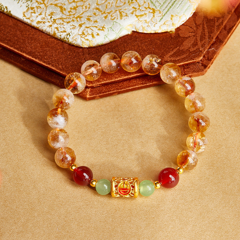 Close up of a citrine and red agate beaded bracelet with a gold tone silver charm on a wrist